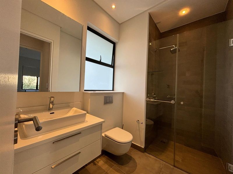 Modern bathroom featuring a wall-mounted vanity with vessel sink, wall-hung toilet with concealed cistern, and a spacious glass-enclosed walk-in shower.