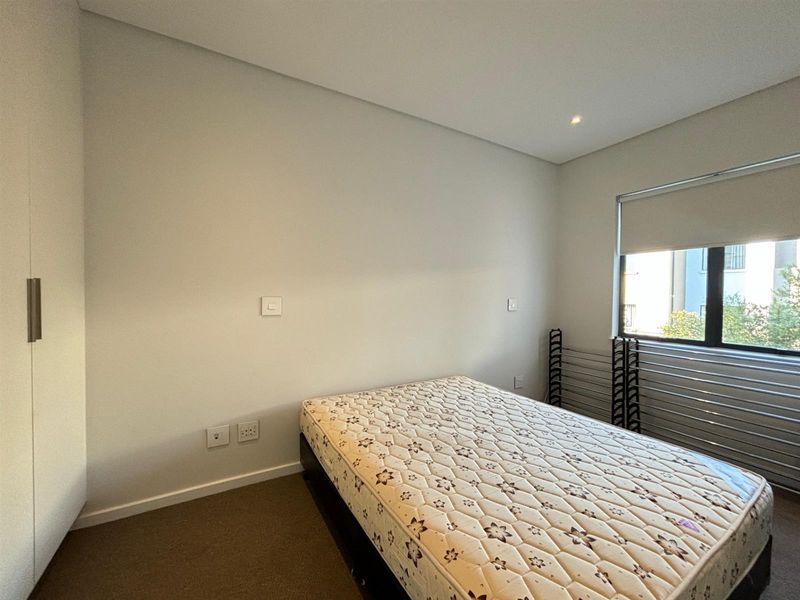 A clean, neutral bedroom featuring built-in wardrobe storage, carpeted flooring, and a roller blind on the window.
