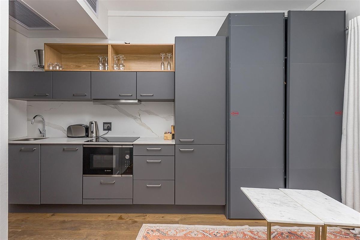 Modern kitchen featuring sleek grey cabinetry, integrated appliances, built-in oven, induction hob, and elegant marble-look splashback with open timber shelving.