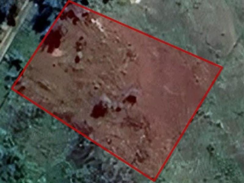 An aerial view of a vacant residential plot of land, highlighted with a red boundary outline.