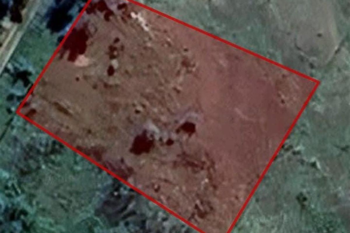 An aerial view of a vacant residential plot of land, highlighted with a red boundary outline.