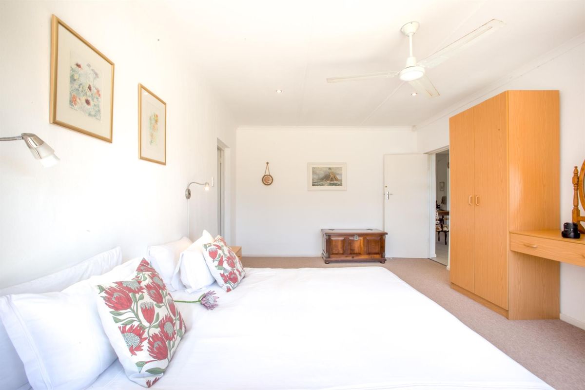 A spacious bedroom featuring neutral carpeting, a built-in wooden wardrobe with integrated vanity, and a ceiling fan.