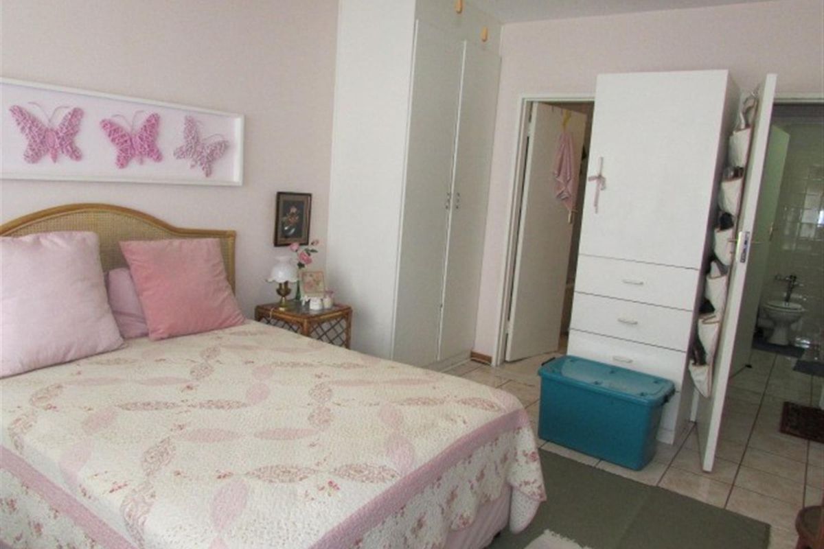 A bedroom featuring built-in cupboards and tiled flooring, with an adjacent view into a bathroom area.