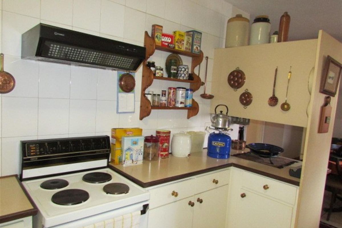 A compact kitchen featuring dated cabinetry, laminate countertops, white wall tiles, and a built-in extractor fan above the electric stove.
