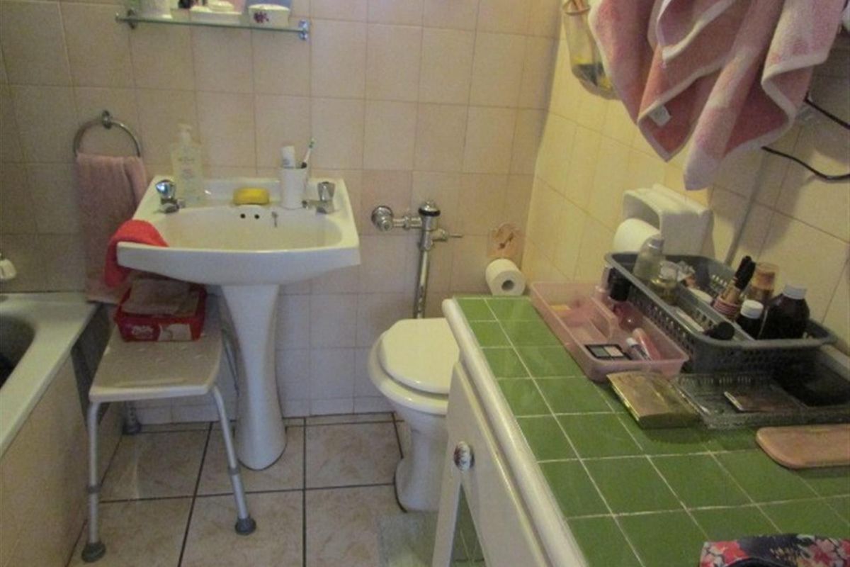 A dated bathroom featuring a pedestal sink, toilet, and tiled vanity area with a bathtub.