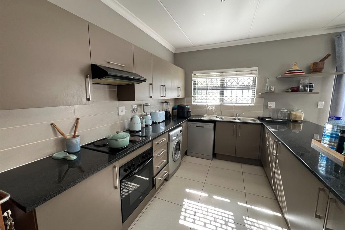Modern kitchen featuring sleek cabinetry, dark granite countertops, integrated oven, hob, extractor fan, and tiled flooring with ample natural light.