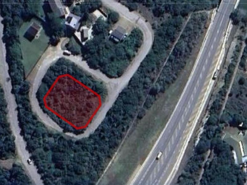 Aerial view of a vacant residential plot highlighted in red, situated within a developed neighborhood near a main road.