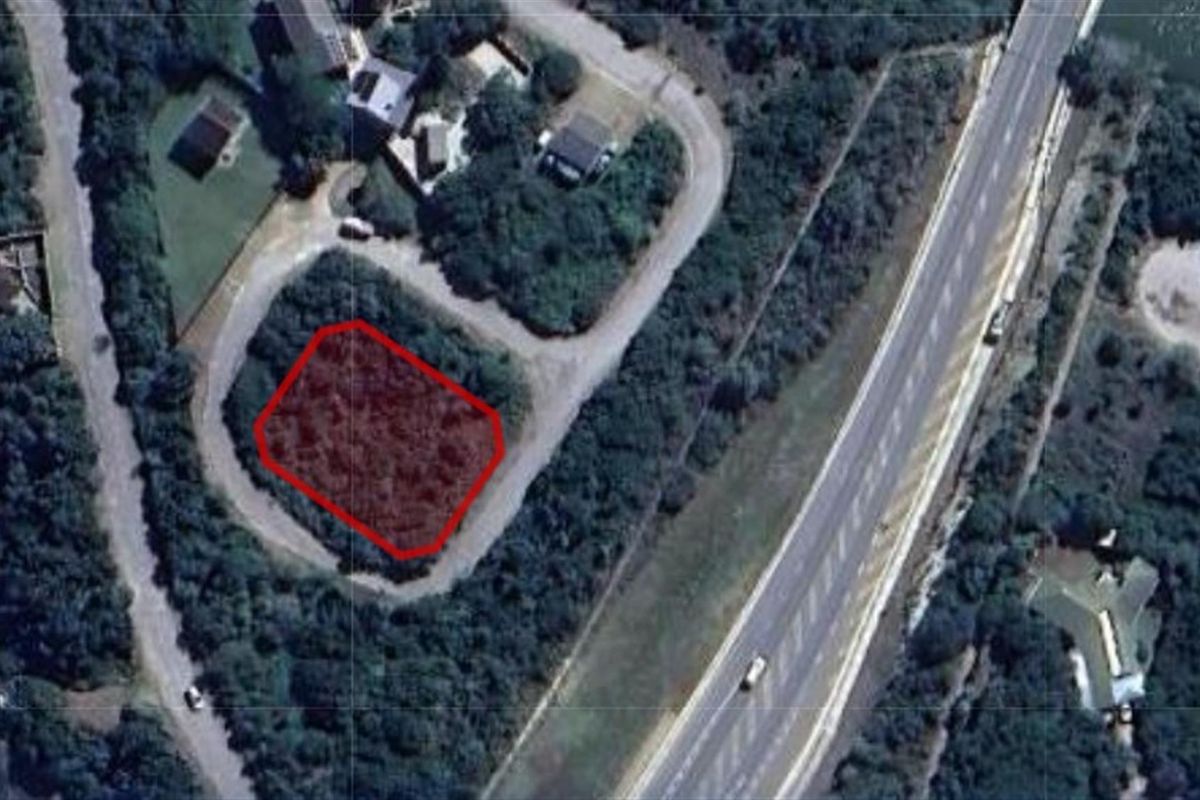 Aerial view of a vacant residential plot highlighted in red, situated within a developed neighborhood near a main road.