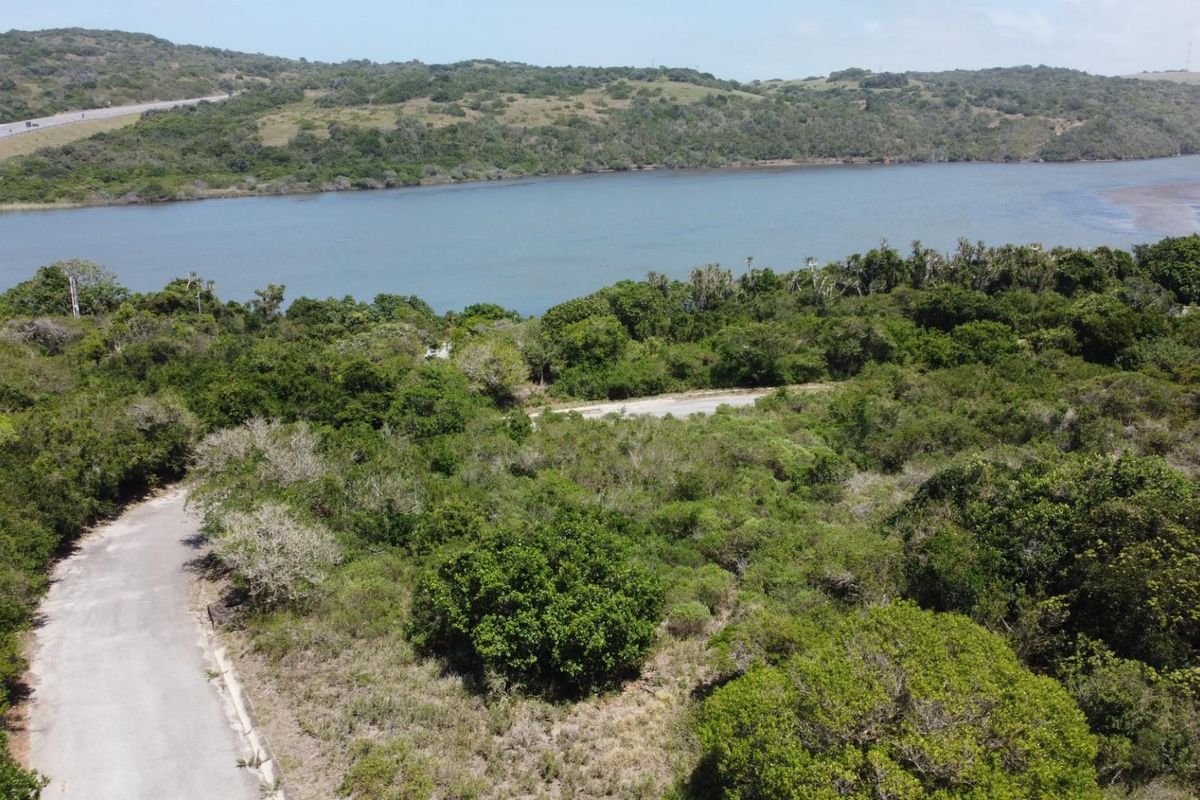 An aerial view of a vacant residential plot featuring natural vegetation, access road, and scenic views of the nearby lagoon and surrounding landscape.