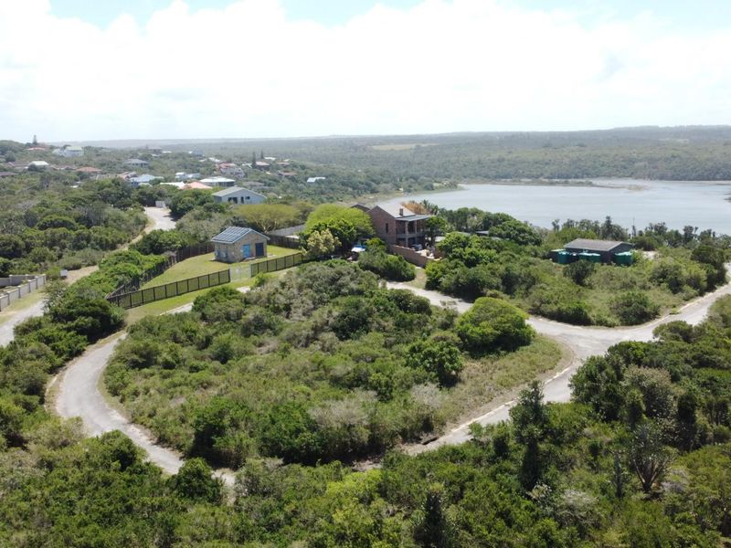 Aerial view of a residential property featuring established vegetation, paved access roads, and existing structures overlooking a scenic lagoon.