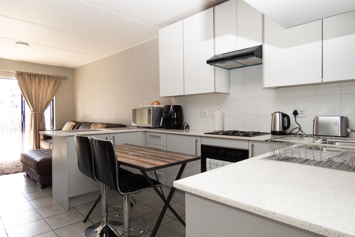Open-plan kitchen featuring white cabinetry, stone-look countertops, built-in hob, and extractor fan, seamlessly flowing into the adjacent living area.