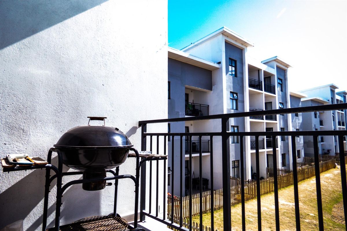 A private balcony featuring a metal railing, overlooking the apartment complex grounds and neighboring building facades.