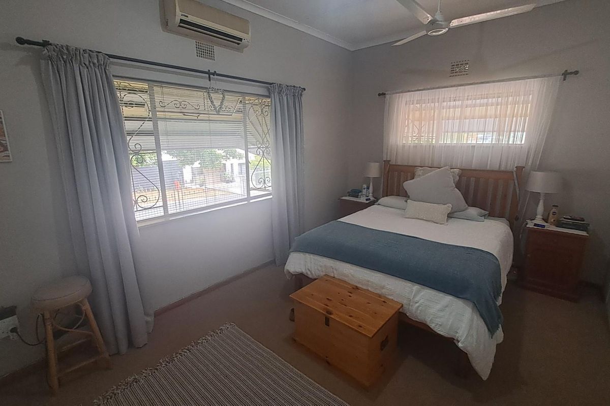 A functional bedroom featuring a ceiling fan, wall-mounted air conditioning unit, and large windows with security bars.