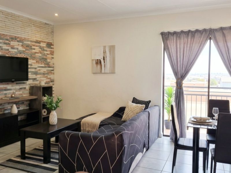 Open-plan living area featuring a stone-cladding accent wall, tiled flooring, and direct access to a private balcony through sliding glass doors.
