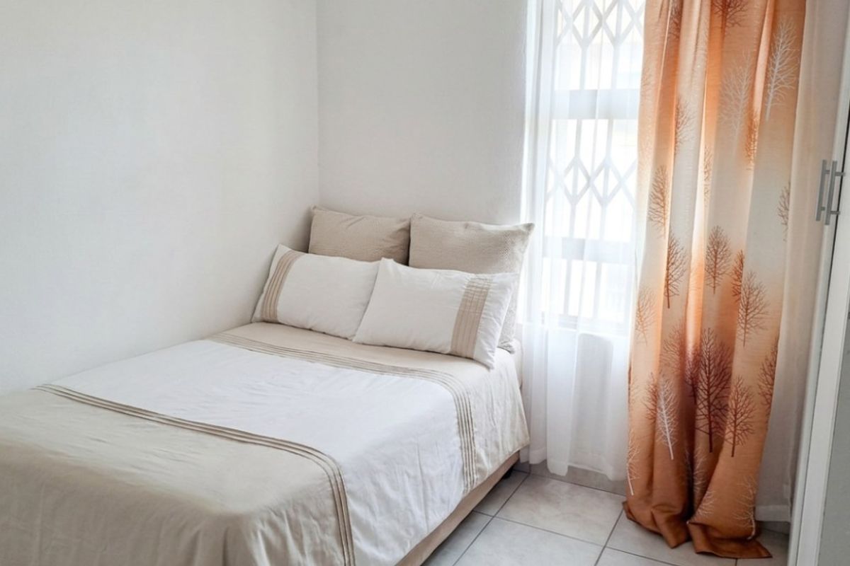 A compact bedroom featuring tiled flooring, a built-in wardrobe, and a window fitted with a security gate.