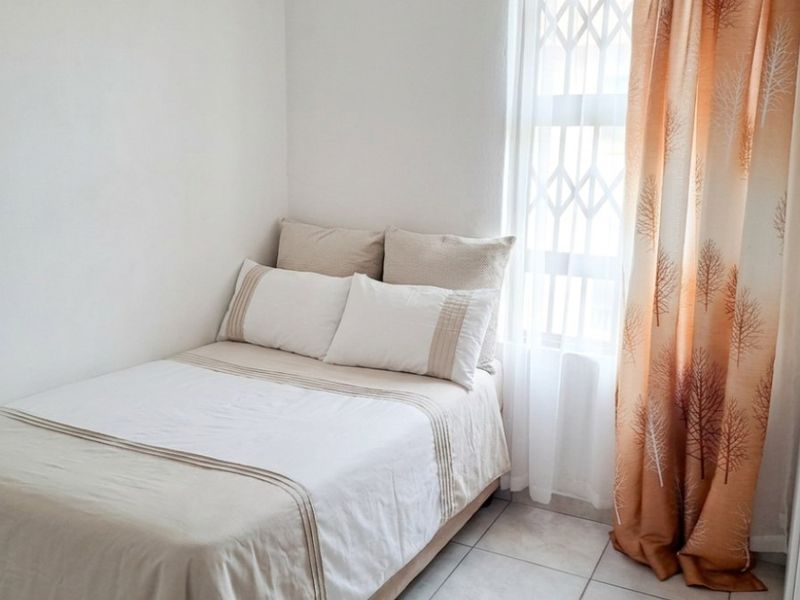 A compact bedroom featuring tiled flooring, a built-in wardrobe, and a window fitted with a security gate.