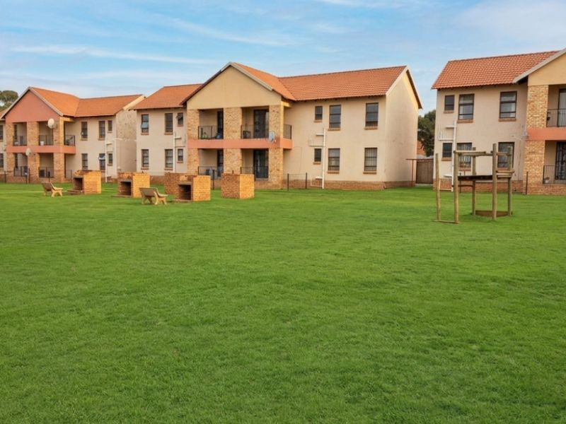 A view of the apartment complex rear facade featuring a large communal lawn area with built-in brick braai facilities and private balconies.