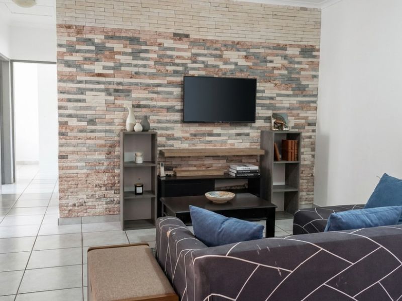 A living room featuring a decorative stone veneer accent wall and neutral ceramic floor tiles, providing a textured focal point for the space.