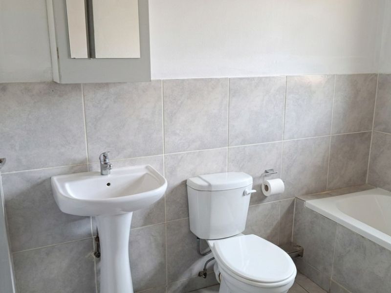 A functional bathroom featuring a pedestal basin, standard toilet, and bathtub with neutral ceramic wall tiling.