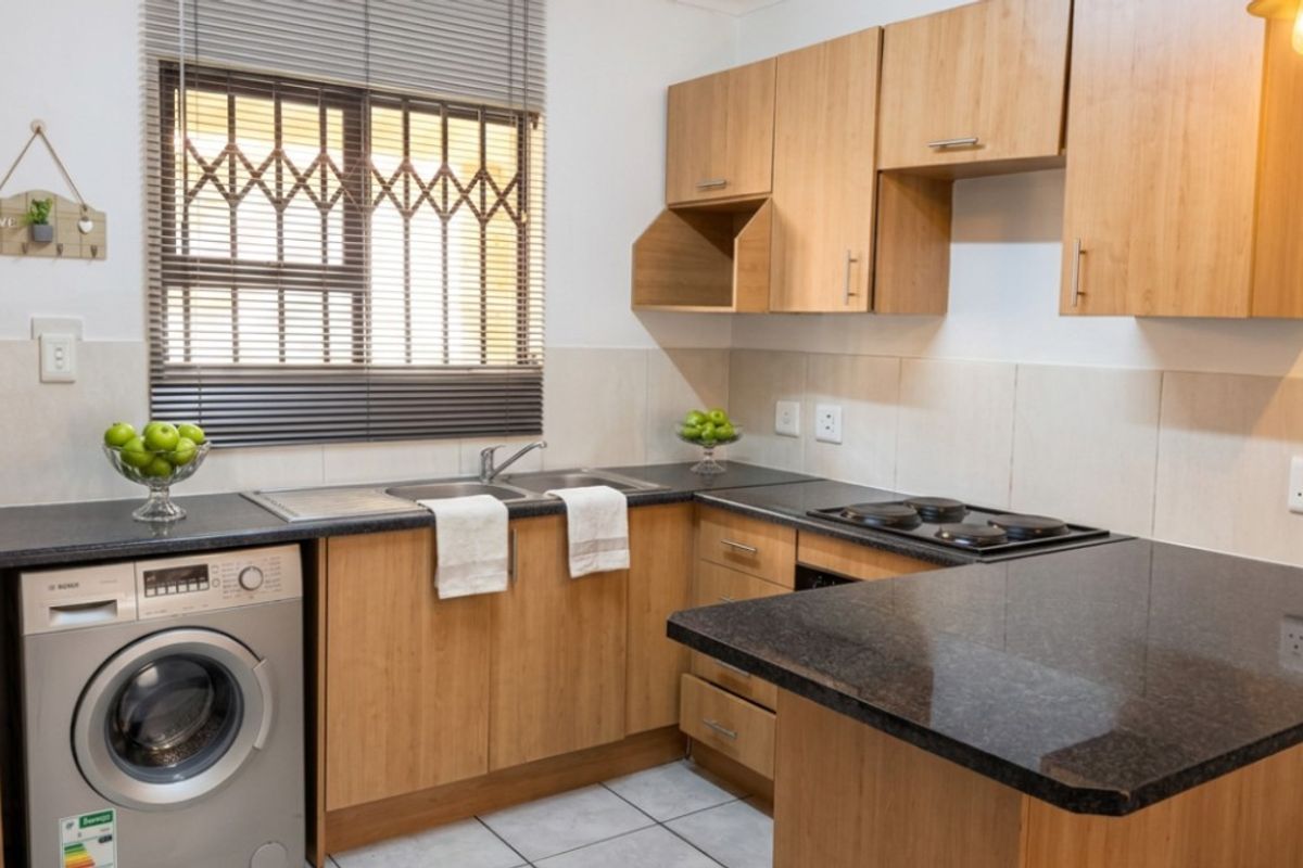 Functional kitchen featuring laminate cabinetry, granite countertops, an electric hob, and tiled flooring, with a built-in space for a washing machine.