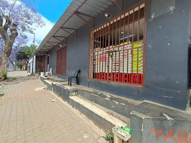 Street-level view of a commercial storefront featuring dark painted walls, metal security gates, and a corrugated roof overhang with concrete steps.