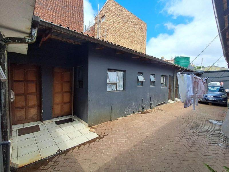 Rear exterior view of a commercial property featuring a paved courtyard, multiple entrance doors, and functional utility areas with exterior wall access.