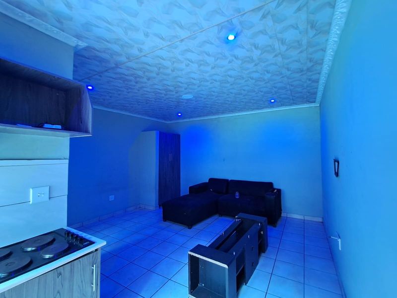 Open-plan living area featuring tiled flooring, built-in kitchen cabinetry with a hob, and decorative ceiling panels with integrated blue accent lighting.