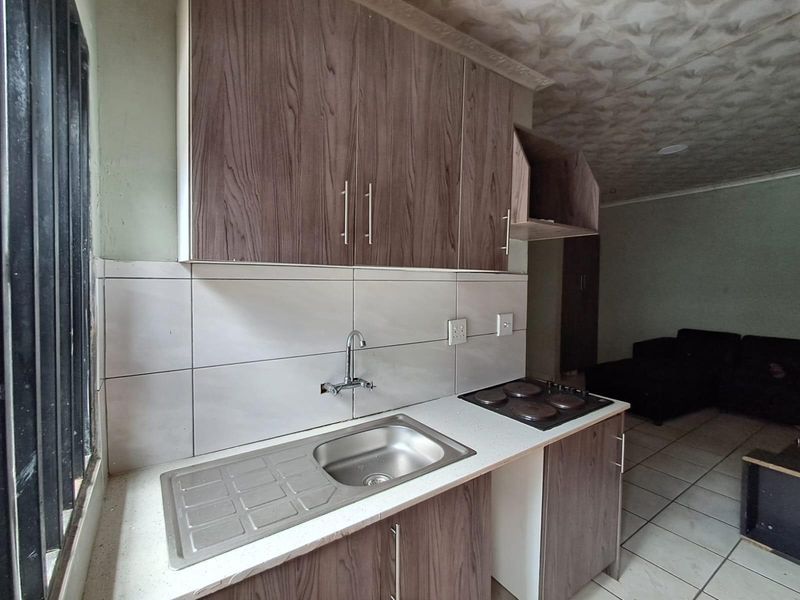 Compact kitchen area featuring wood-look cabinetry, a stainless steel sink, and an integrated electric hob with tiled backsplash and flooring.