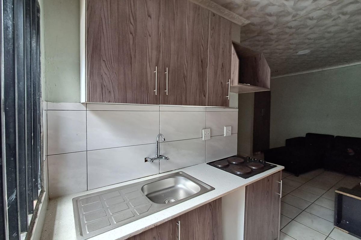 Compact kitchen area featuring wood-look cabinetry, a stainless steel sink, and an integrated electric hob with tiled backsplash and flooring.