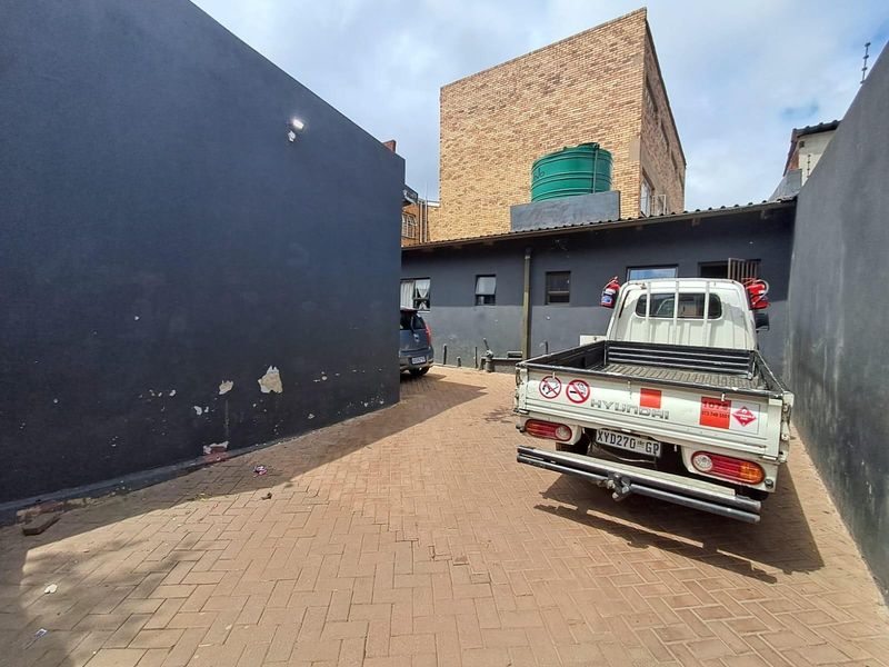 Rear exterior area featuring a paved driveway, water storage tank, and dark painted walls showing signs of surface wear and paint deterioration.