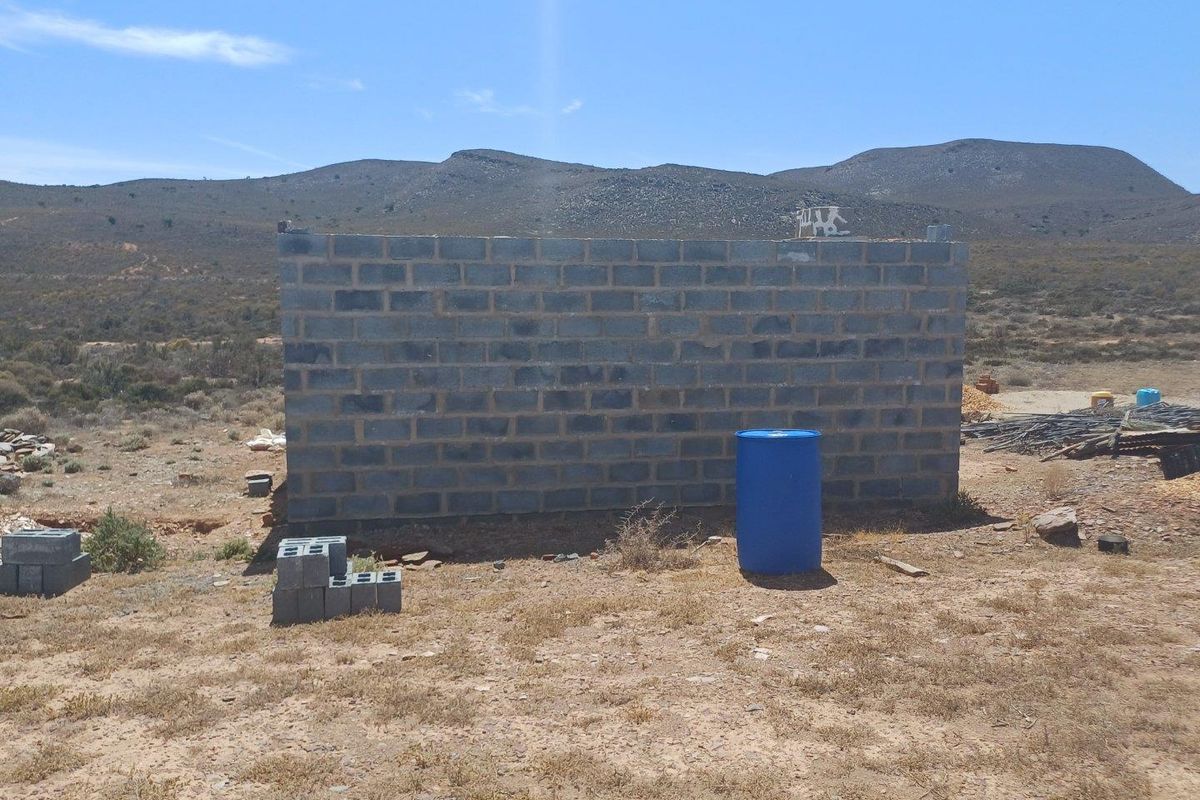 An unfinished concrete block structure situated on a rural farm property, showing early stages of construction.