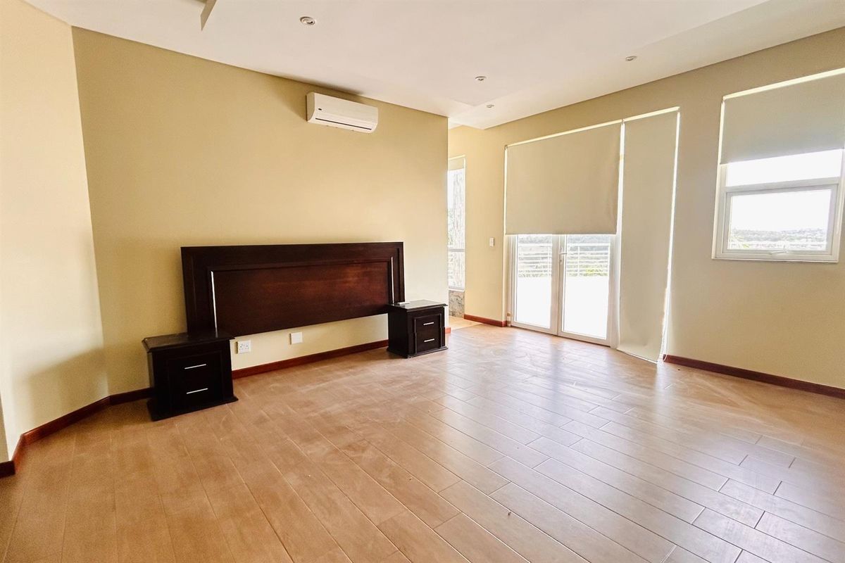 Spacious bedroom featuring wood-look tile flooring, wall-mounted air conditioning unit, and glass sliding doors leading to an outdoor area.