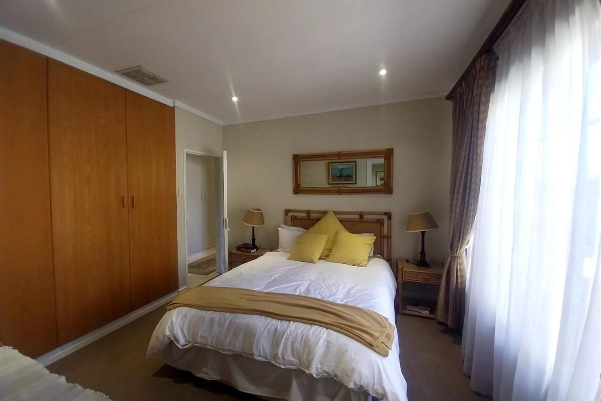 A well-maintained bedroom featuring built-in wooden cupboards, recessed downlighting, and large windows with curtains, providing a comfortable and functional living space.