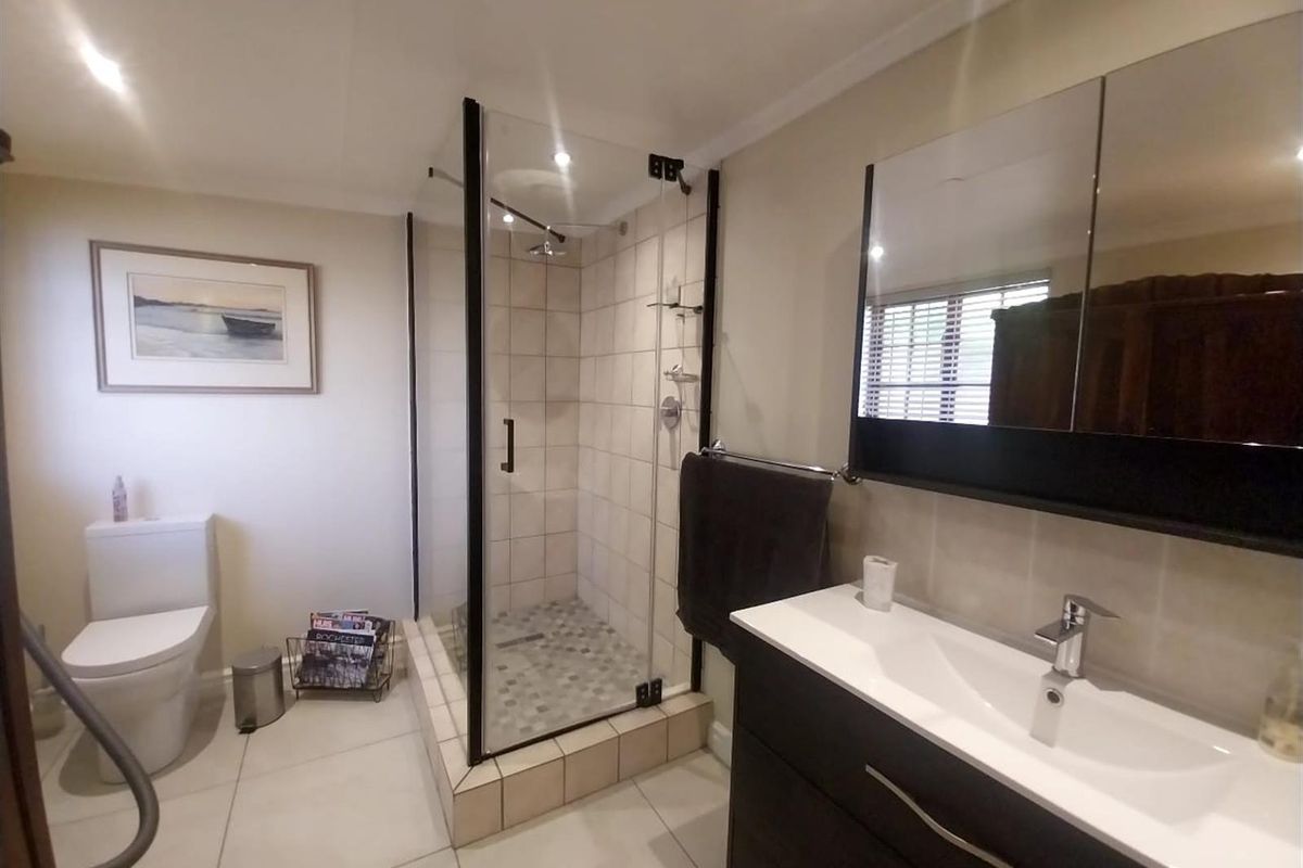Modern bathroom featuring a glass-enclosed shower with tiled flooring, a contemporary vanity with integrated basin, and a sleek toilet.