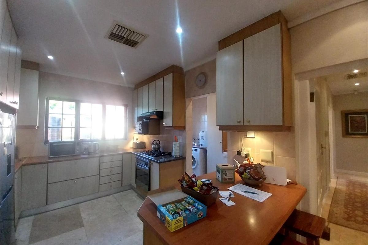 Functional kitchen featuring built-in cabinetry, integrated oven and hob, and a breakfast bar, with an adjacent scullery area.