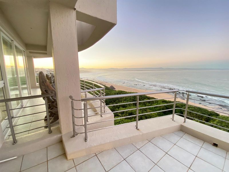 Spacious covered balcony featuring tiled flooring and stainless steel balustrades, offering panoramic ocean and beach views.