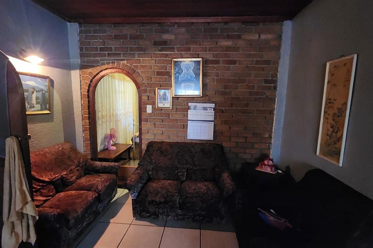 A living room featuring a rustic exposed brick feature wall with an arched doorway leading to an adjacent space and tiled flooring.