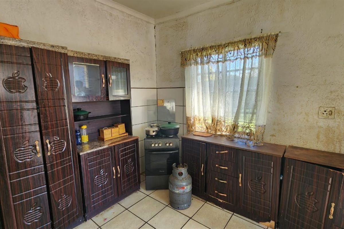 A dated kitchen featuring dark wood-finish cabinetry, tiled flooring, and a freestanding gas stove, requiring significant cosmetic renovation and wall repairs.