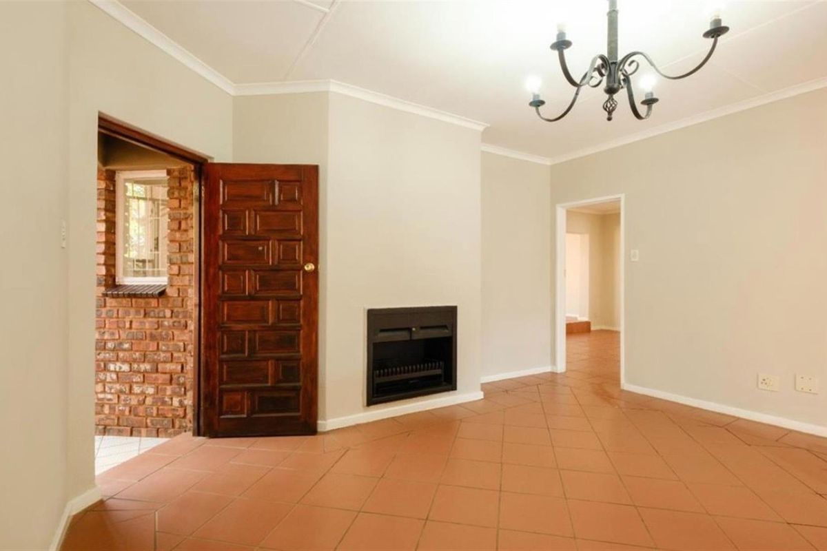 A spacious living room featuring terracotta floor tiles, a built-in fireplace, and a classic chandelier, leading to an exterior brick-walled entrance.