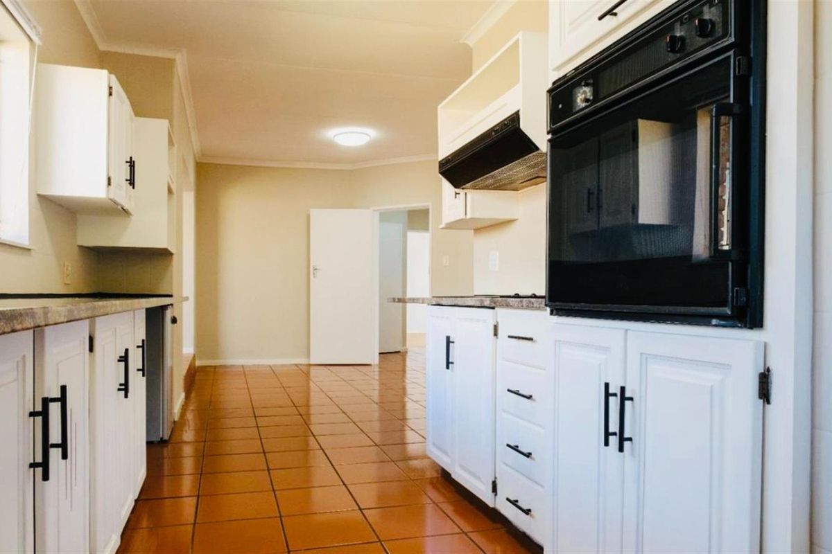 A functional kitchen featuring white cabinetry, built-in oven, extractor fan, and tiled flooring, offering a clean and practical workspace.