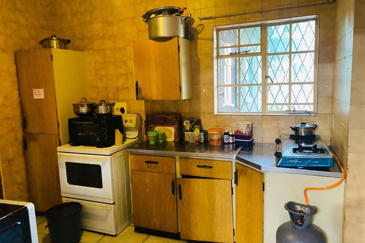 A dated kitchen featuring original wooden cabinetry, tiled walls, and a functional layout with a gas stove and built-in storage.