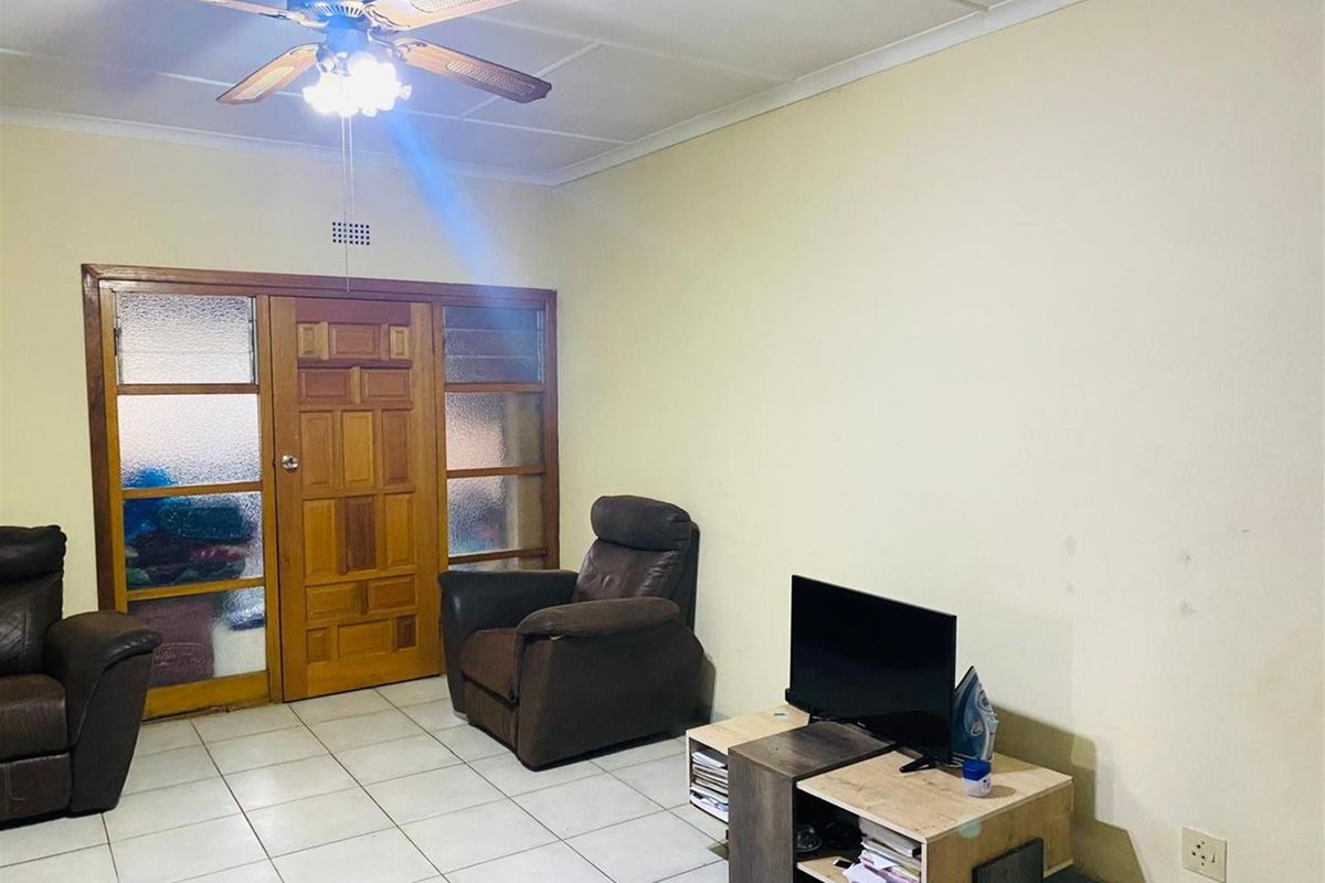 A living room featuring tiled flooring, a ceiling fan, and a wooden entrance door with glass side panels.