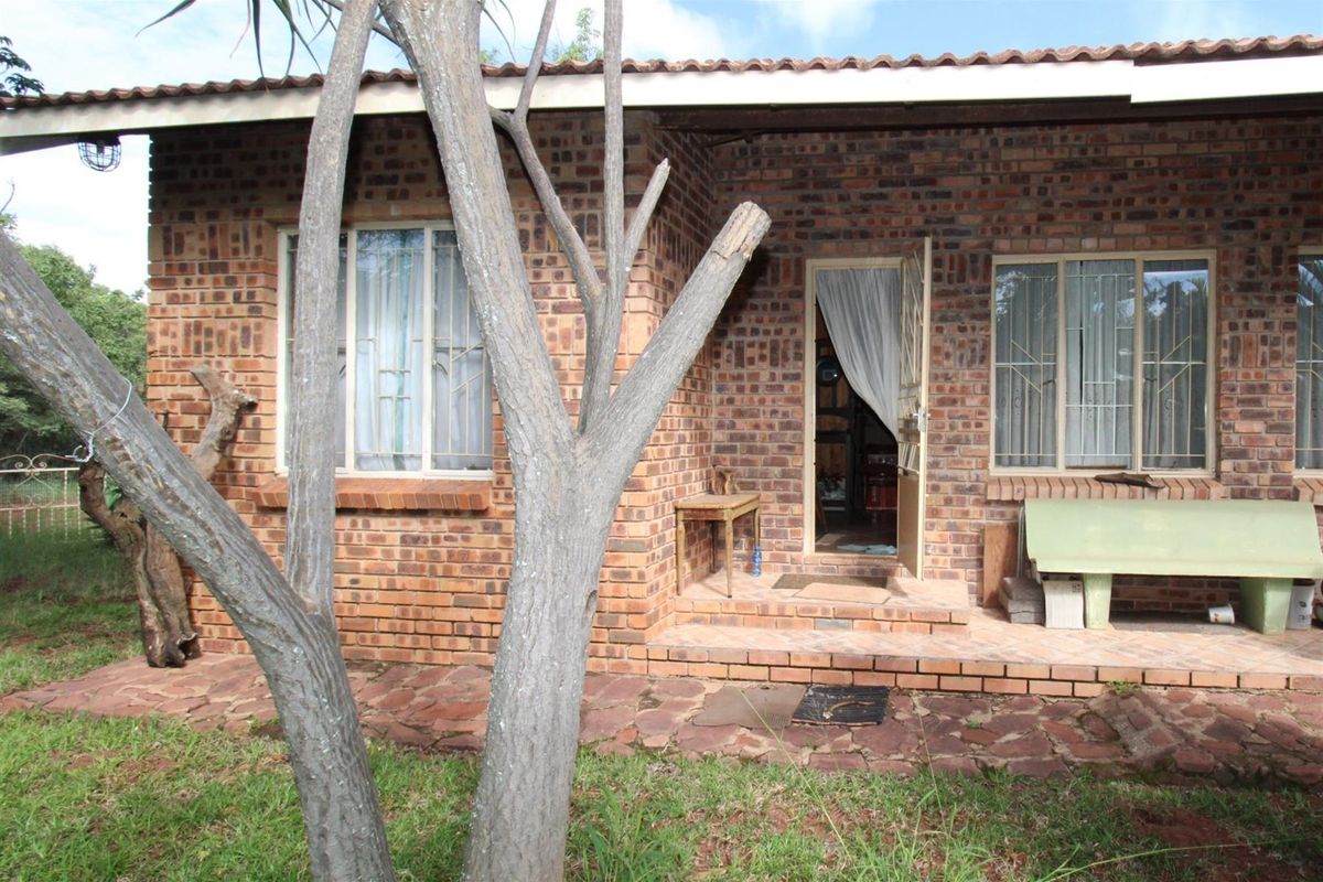 Rear exterior view of a face brick farm dwelling featuring a stone paved patio, metal window frames with security bars, and a tiled roof.