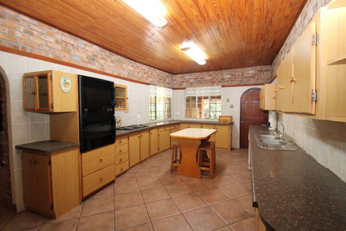 A spacious kitchen featuring timber ceilings, exposed brick walls, tiled flooring, built-in cabinetry, and integrated cooking appliances.