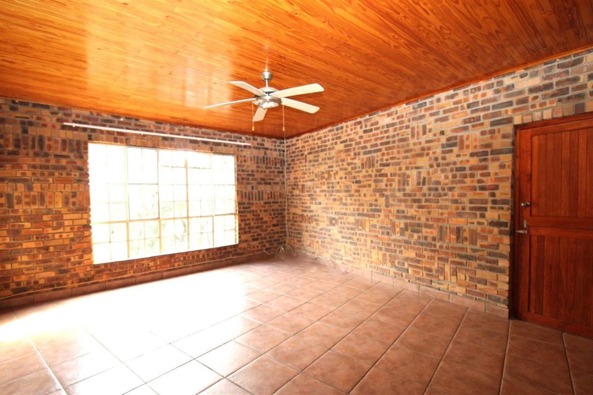 Spacious living area featuring exposed brick walls, a warm timber ceiling, tiled flooring, and a ceiling fan.