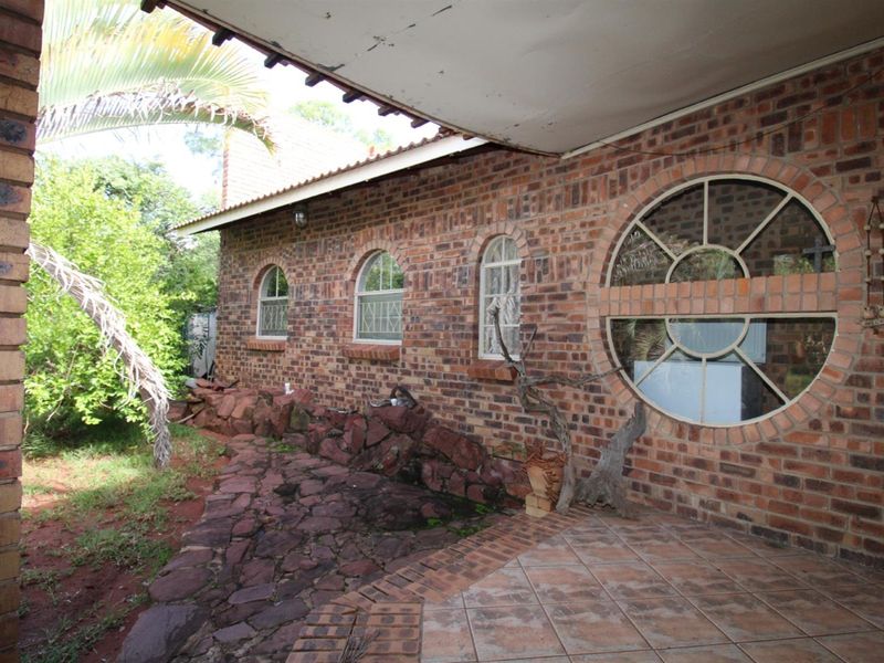 A covered patio area featuring exposed brick walls, arched windows, a unique circular window, and tiled flooring leading to a stone garden path.
