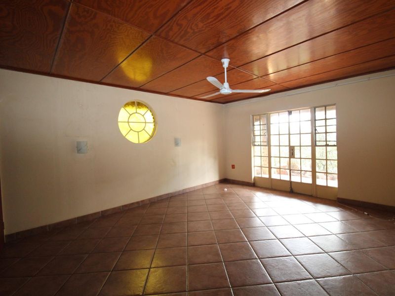 Spacious living area featuring a wooden panelled ceiling, tiled flooring, a unique circular window, and glass french doors leading to the exterior.
