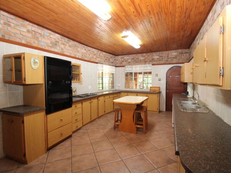 A spacious kitchen featuring timber ceilings, exposed brick walls, tiled flooring, built-in cabinetry, and integrated cooking appliances.