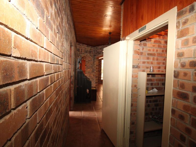 A rustic hallway featuring exposed brick walls, a warm timber ceiling, and tiled flooring, leading to an adjacent storage or utility space.