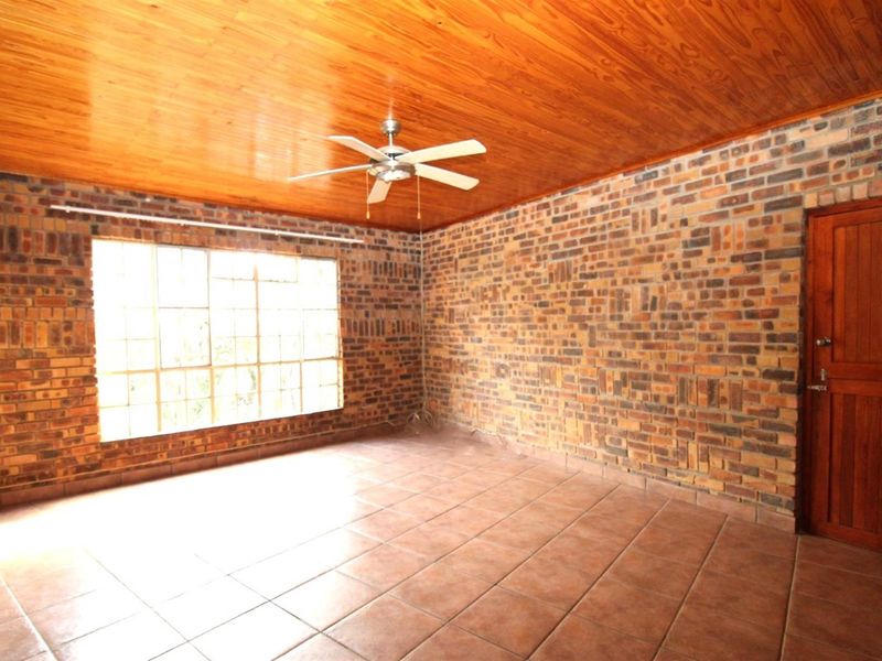 Spacious living area featuring exposed brick walls, a warm timber ceiling, tiled flooring, and a ceiling fan.